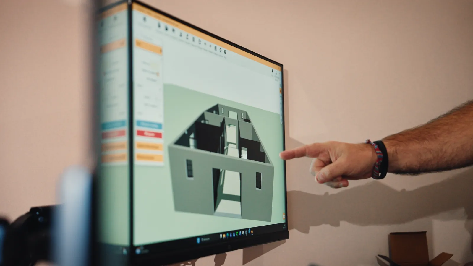 Une main désigne la maquette 3D d’une maison sur un écran.