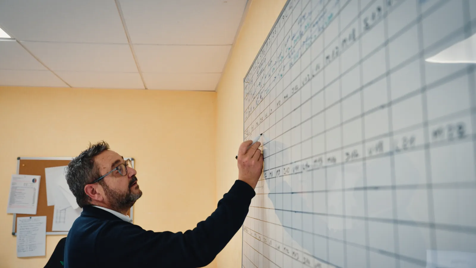 Un homme note une intervention sur un grand planning mural.