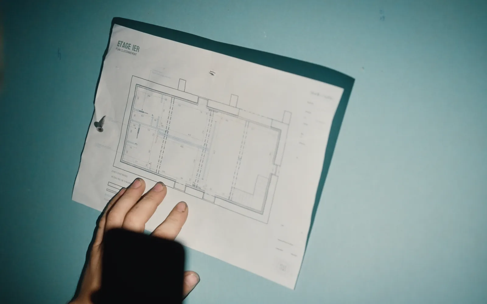Une main tient le plan de l’étage devant un mur en plaques de plâtre hydrofuges, sur un chantier.