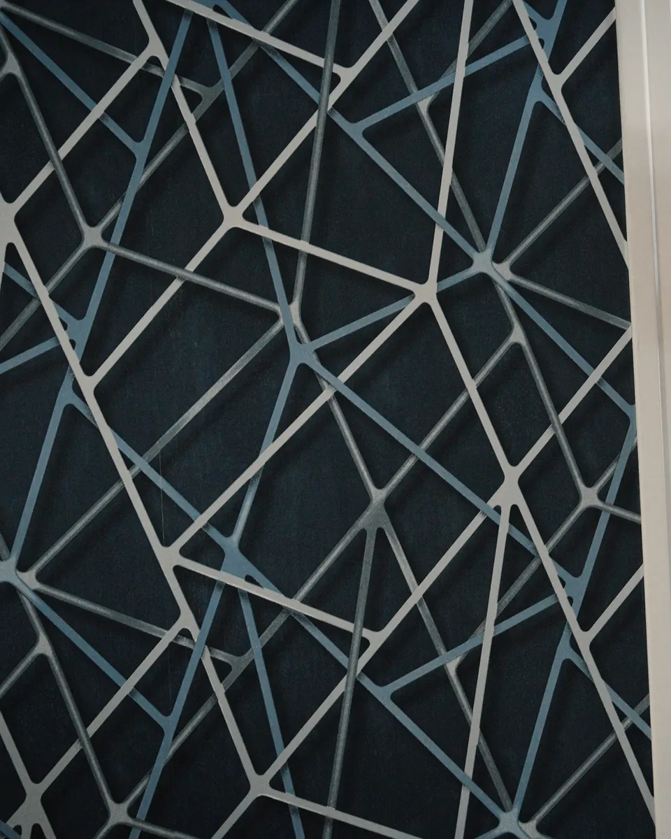 Détail d’un panneau mural décoratif : des lignes blanches en relief qui se croisent sur un fond bleu nuit.
