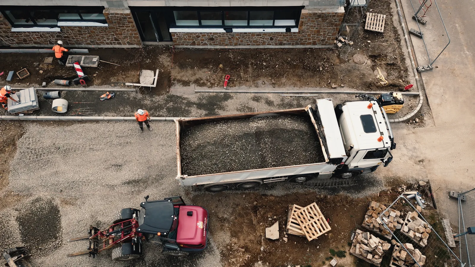 Vue du ciel d’un chantier de bâtiment : camion, mini-dumper et compagnons qui posent des bordures.