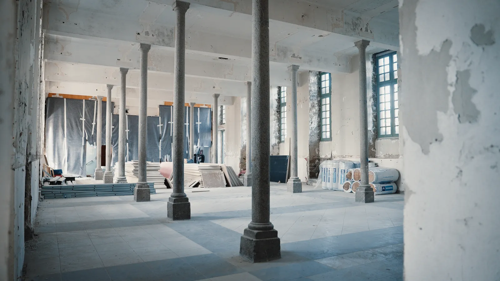 Grande salle à colonnes de fonte en réhabilitation, sous de hautes fenêtres.