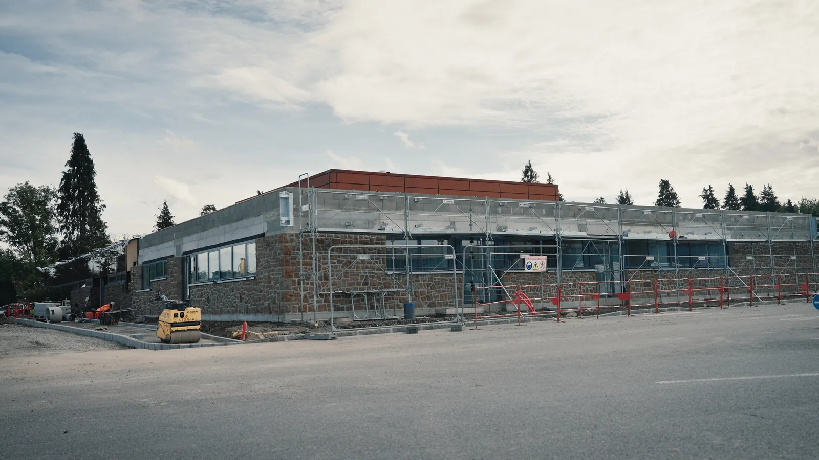Bâtiment de plain-pied en pierre sous échafaudage, avec un rouleau compacteur jaune sur le chantier.