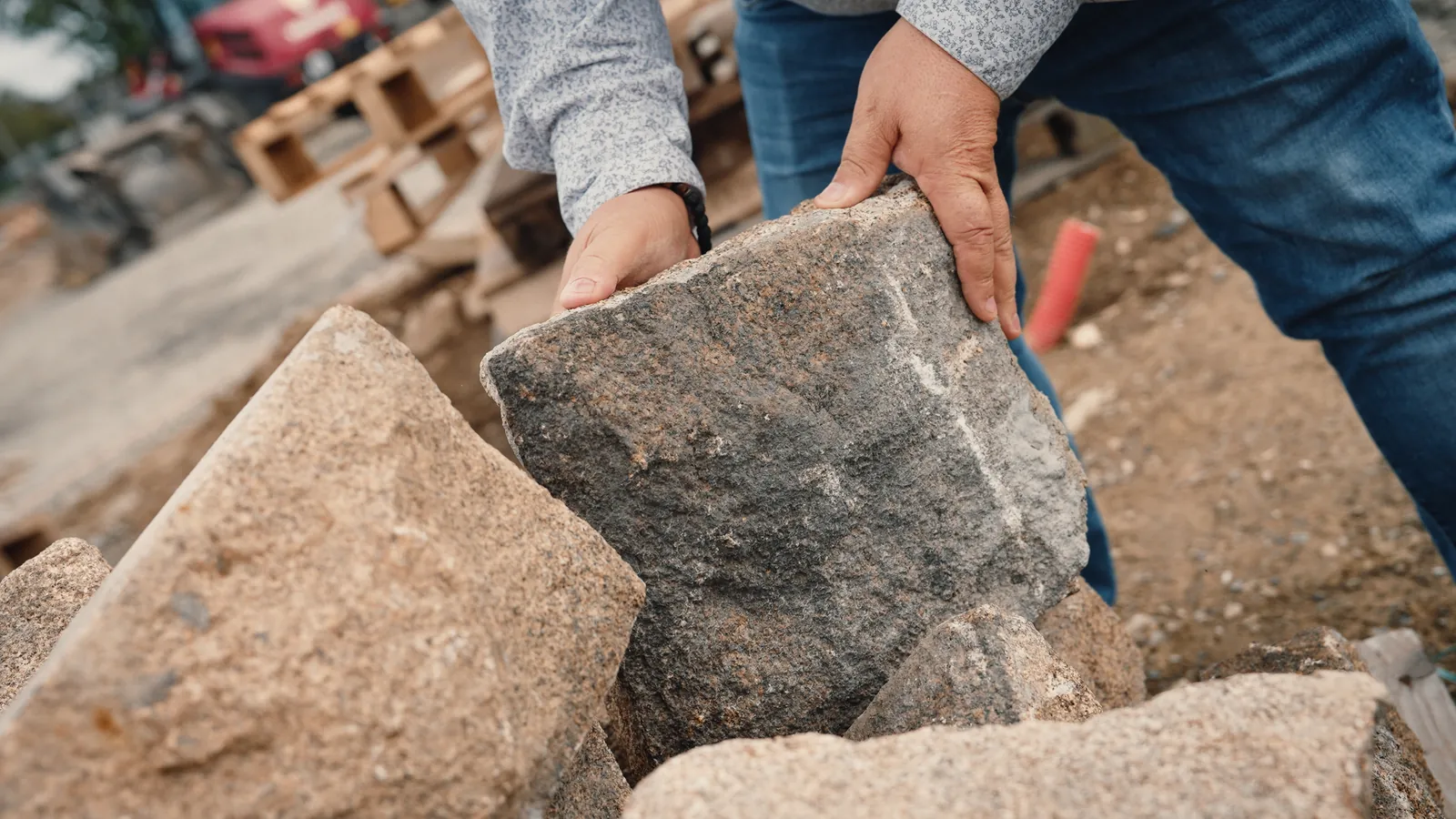 Des mains soulèvent un moellon de granit.