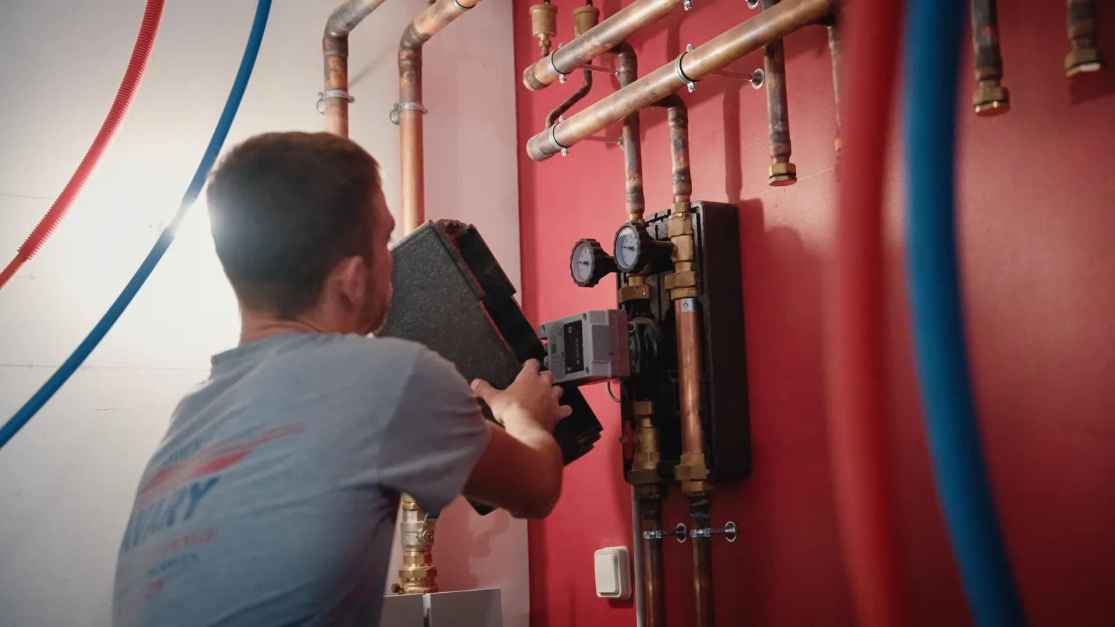 Chaufferie au mur rouge : module posé, tubes de cuivre et manomètres.