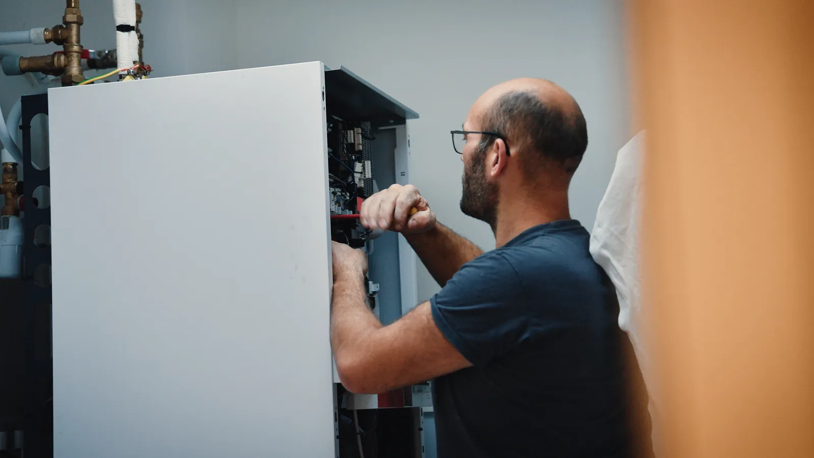 Un technicien intervient au tournevis dans le coffret électrique du module intérieur d’une pompe à chaleur.